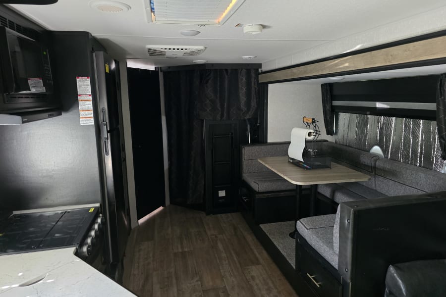 Spacious RV rental interior features a kitchen area, dining booth, and living space with hardwood flooring, ideal for travel.