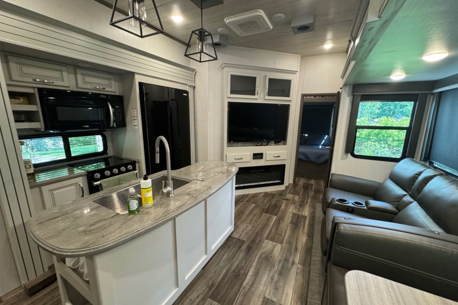 Modern RV rental interior: kitchen island, living room sofa, TV, and fireplace. Wood floors, bright space.