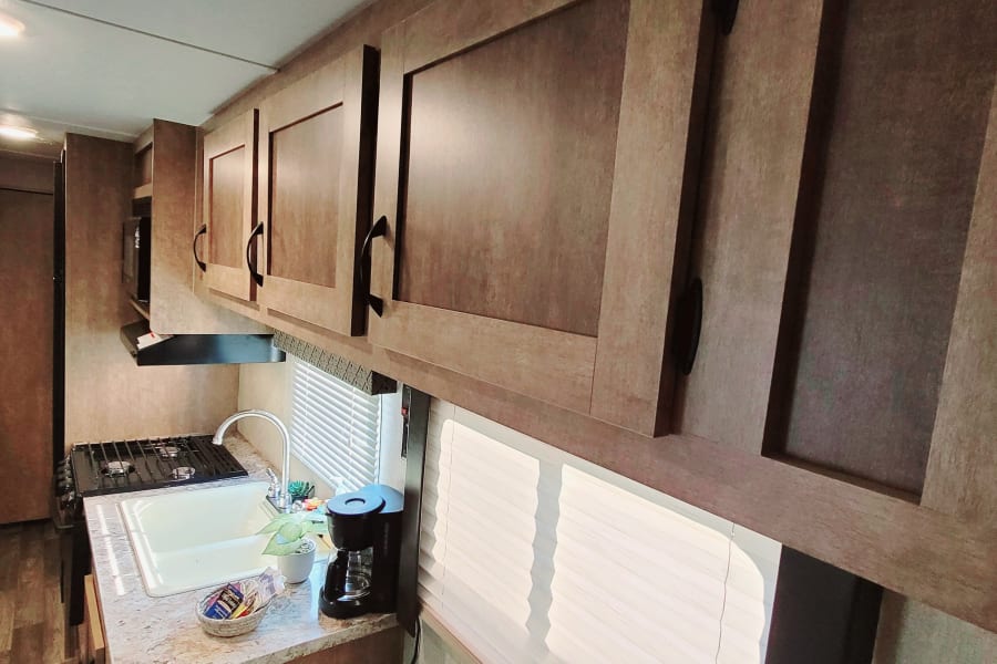 RV rental: Interior view of an RV, showing kitchen with sink, stove, cabinets, and bunk beds in background.