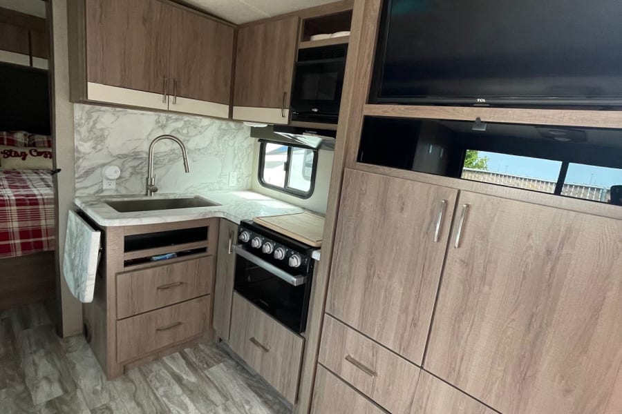 Modern RV rental interior showcasing a well-equipped kitchen with sink, stove, and microwave, plus cozy bedroom area.