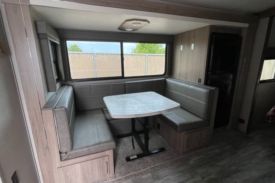 RV rental dinette with U-shaped seating, table, and refrigerator. Ideal for travel trailer living.