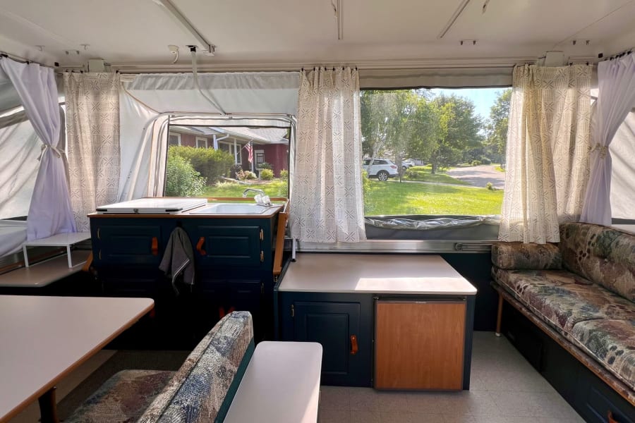 Pop-up RV rental interior: bright, compact space with kitchenette, dinette, and sofa seating for cozy travels.