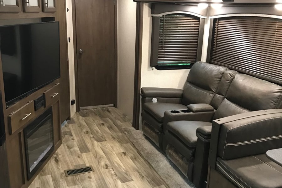 Inside this **rv rental**: a modern living space with comfy recliners, TV, electric fireplace, and wood-look flooring.