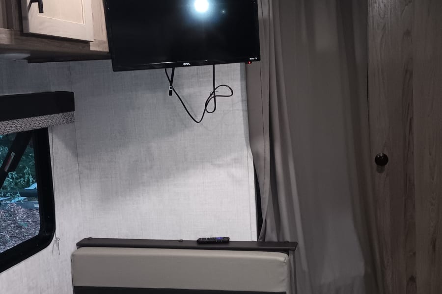 An RV rental's interior, featuring a dinette table, comfy seating, wall-mounted TV, and privacy curtain.