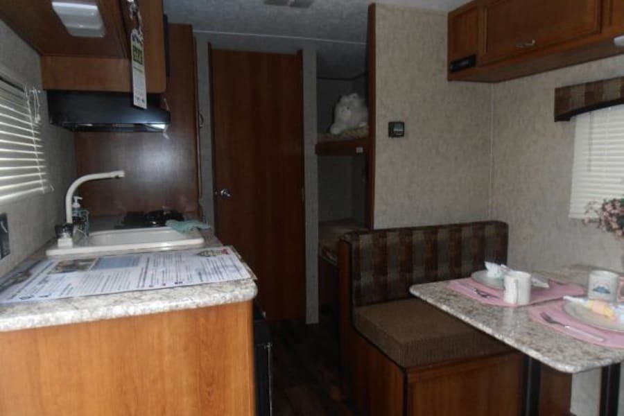 Inside this RV rental: a compact kitchen with sink, a dining booth, and peek of bunk beds, ideal for travel.