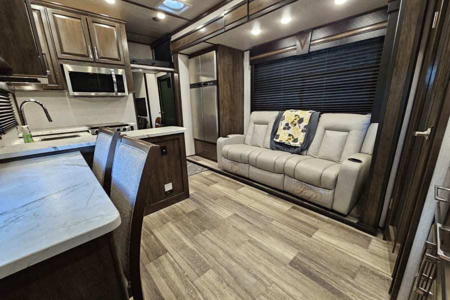 Modern RV rental interior with full kitchen, dining area, refrigerator, and comfy living room sofa.