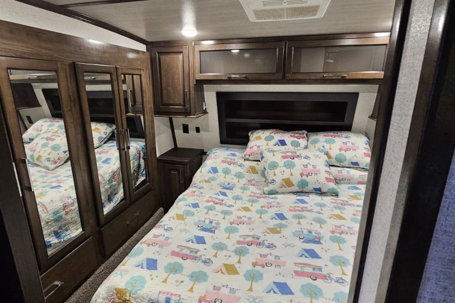 Cozy RV rental bedroom featuring a full bed with a fun camping quilt, dark wood cabinets, and mirrored closet.