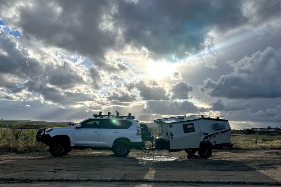 Overland SUV towing a Cricket camper, ideal for your next rv rental adventure. Dramatic clouds with sun rays on a dirt road.