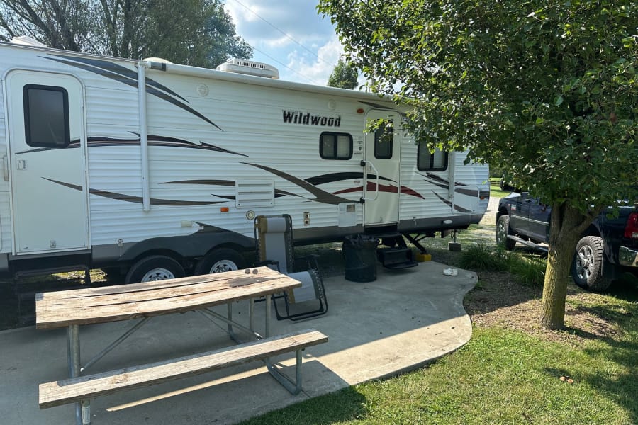Spacious RV rental parked at a shady campsite with a picnic table, perfect for outdoor adventures.