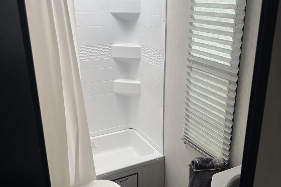 Compact and functional RV rental bathroom featuring a shower-tub, toilet, and sink, designed for comfort on the go.