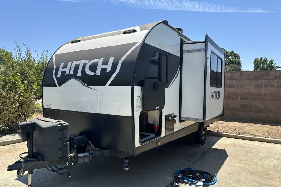 A clean white and black "HITCH" travel trailer, perfect for an RV rental adventure, parked on concrete under a blue sky.