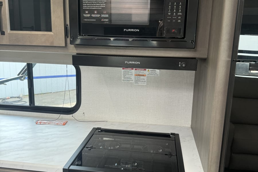 RV rental kitchen: Furrion microwave with air fryer, cooktop, & cabinets. Modern, compact appliances for travel.
