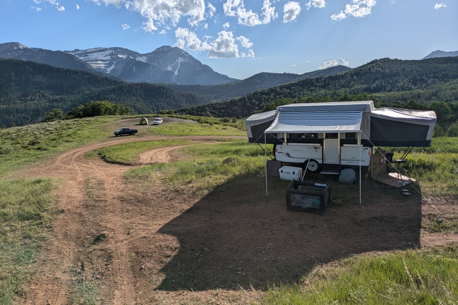Enjoy mountain views with your RV rental. This pop-up camper is set up for a family camping trip, with a truck and tent nearby.