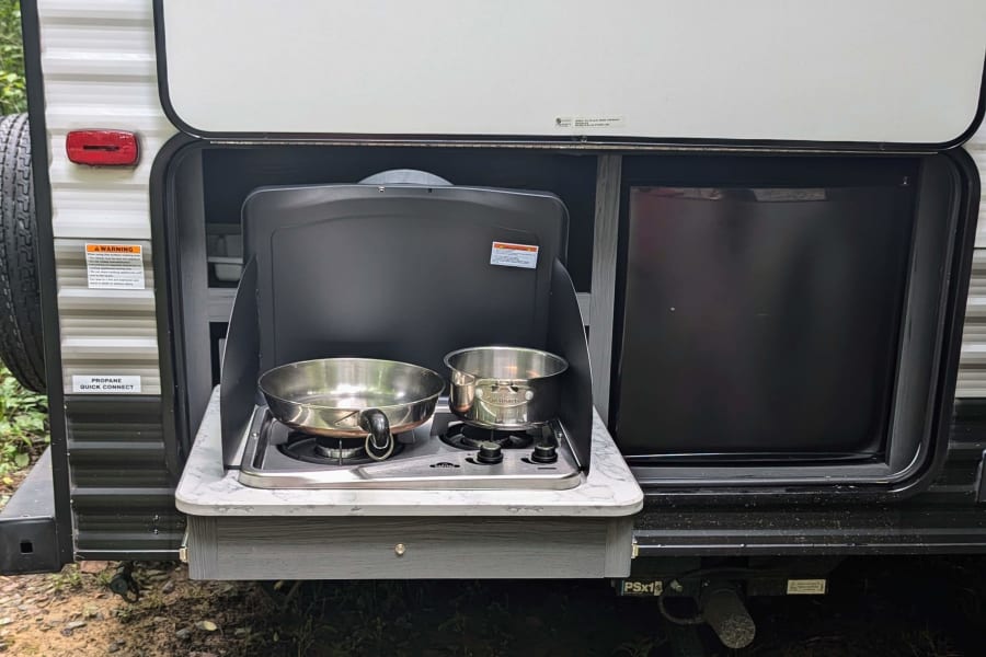 This RV rental features a pull-out outdoor kitchen with a two-burner stove, pan, pot, and mini-fridge for easy camping meals.