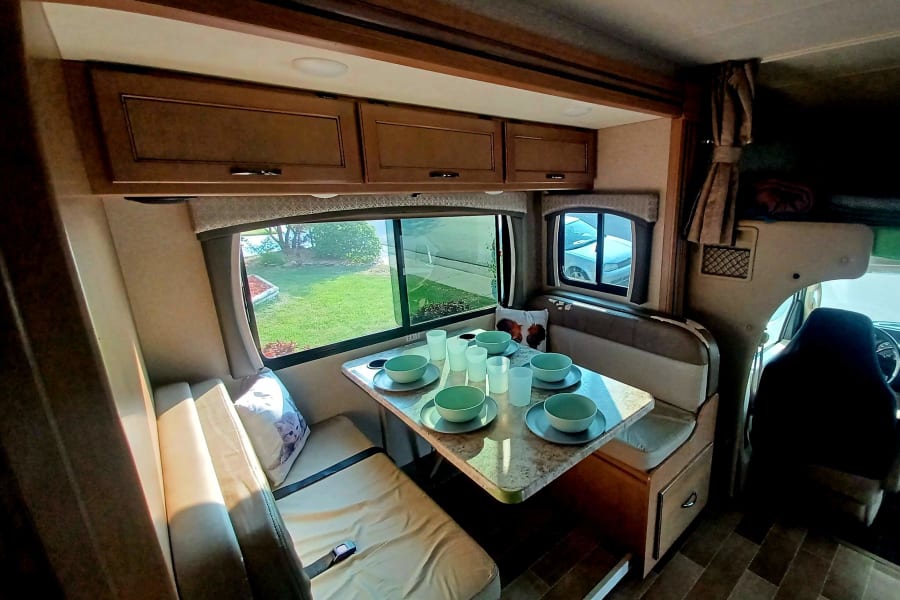 Bright RV rental interior: A cozy dinette with place settings, scenic window views, and ample storage, perfect for travel.