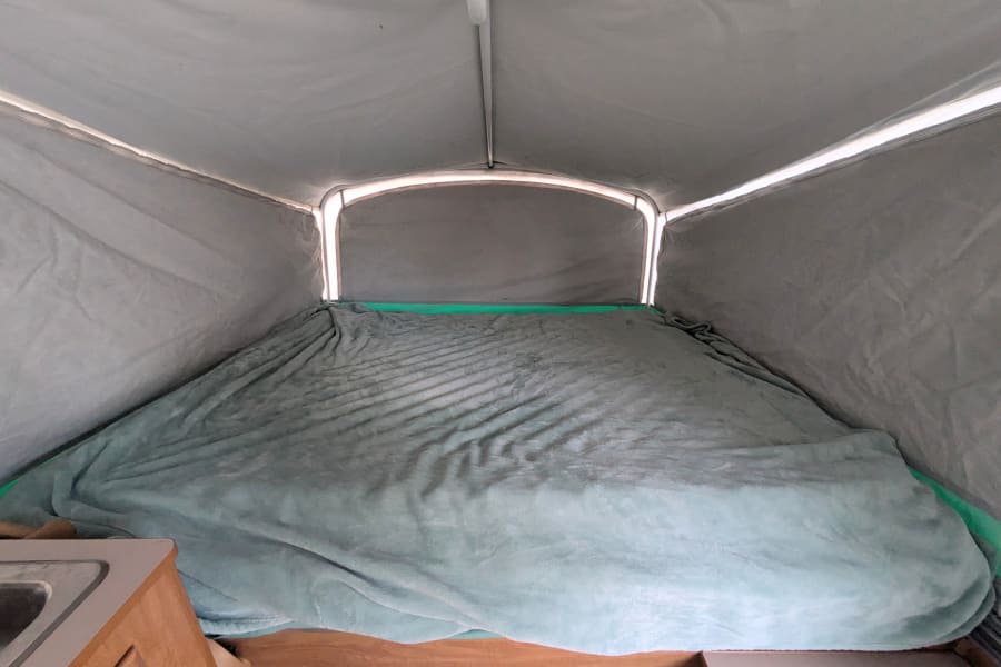 Inside an RV rental pop-up camper, featuring a spacious sleeping area with a soft blanket and bright canvas walls.