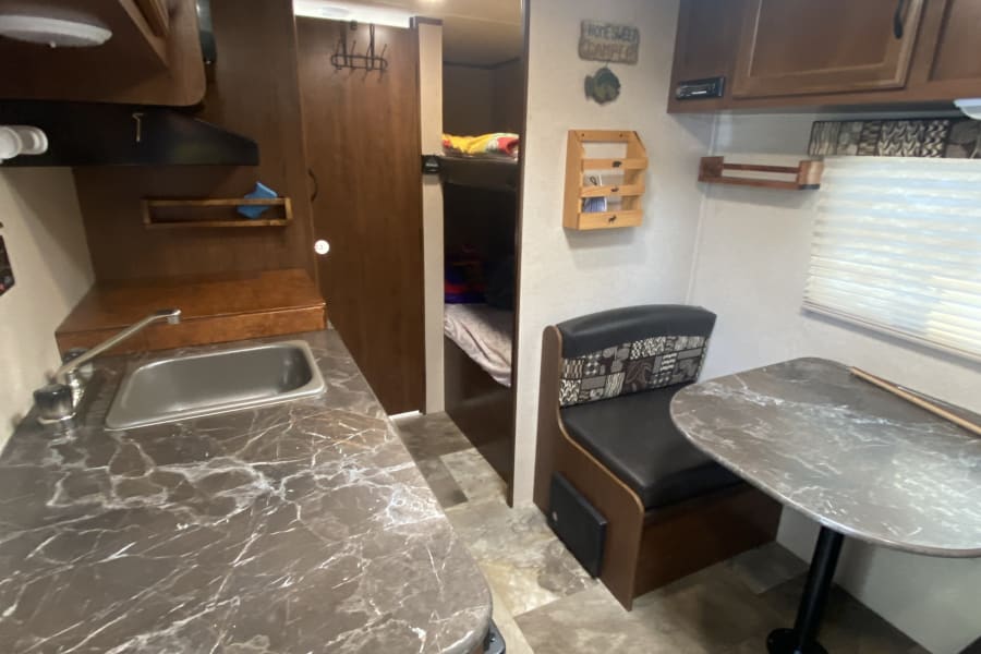**RV rental** interior, featuring a kitchen, dining booth, and bunk beds, offering a cozy living space for travelers.