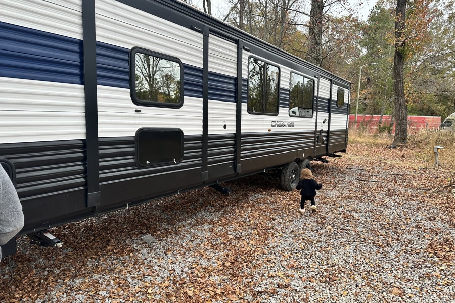 RV rental ready for adventure: A child plays outside the large travel trailer on a gravel lot filled with autumn leaves.