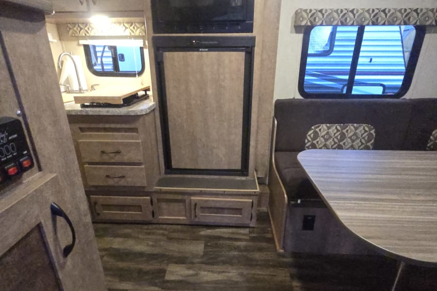 Compact RV rental interior featuring a functional kitchen, microwave, fridge, and cozy dinette area with patterned cushions.