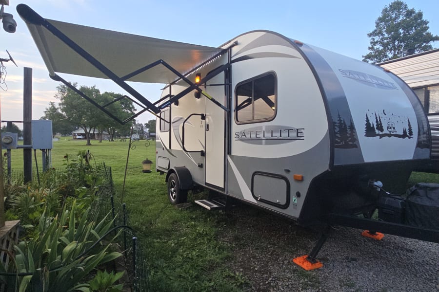 Experience our Satellite travel trailer RV rental, lights on and awning out, ready for your camping adventure.