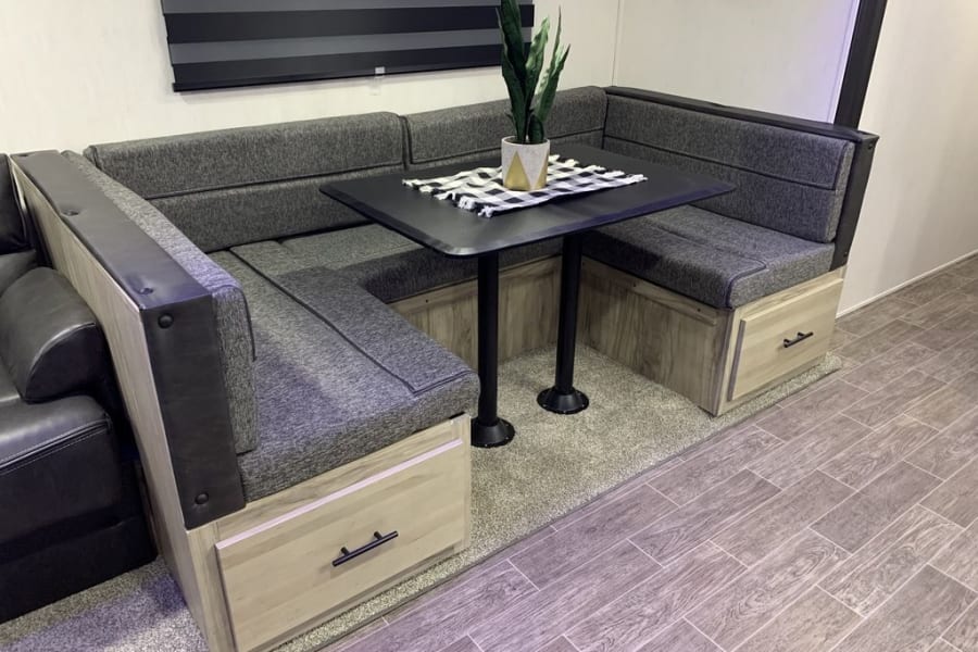 Spacious RV rental U-shaped dinette with comfortable gray seating, storage drawers, and a black table for meals.