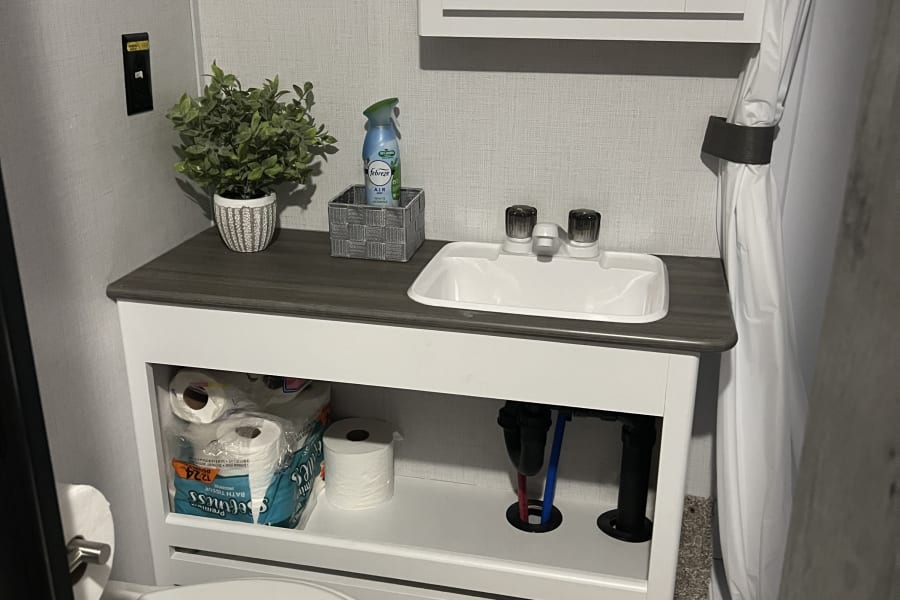 Compact RV rental bathroom with a sink, toilet, and shower, equipped with essential amenities.