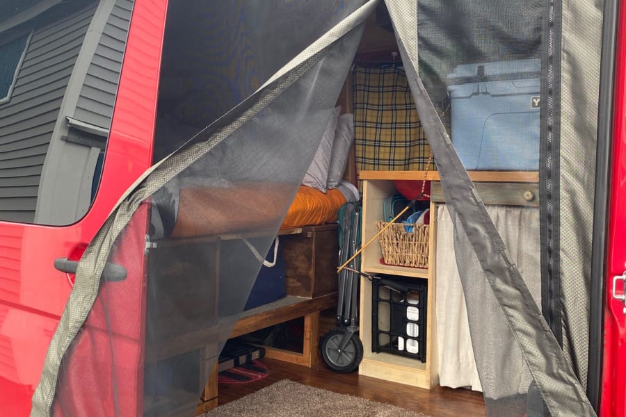 Inside an rv rental camper van: mesh screen door open to reveal organized storage, wood floor, and cozy interior details.