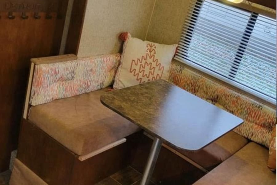 Bright RV rental interior showing a cozy dinette with U-shaped seating, central table, and window with blinds.