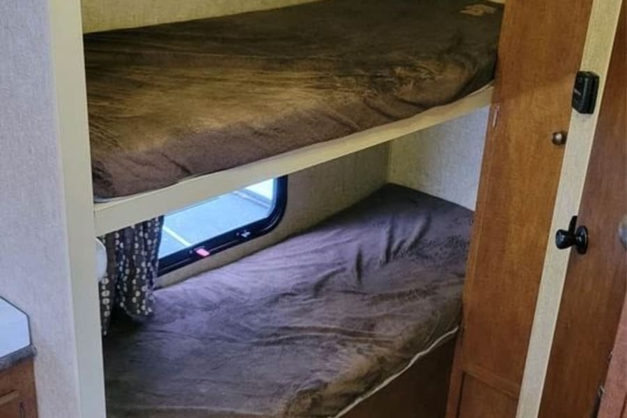 Cozy RV rental bunk beds, two dark brown sleeping areas one above the other, with a window in a compact RV interior.