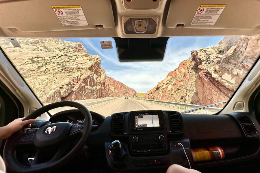 Road trip adventure in an RV rental, navigating breathtaking red rock canyons. Driver's view of highway and navigation display.