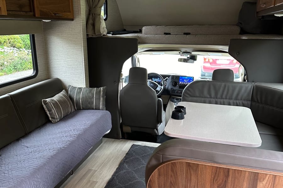 Explore this inviting RV rental interior: comfortable dinette, sofa, and overhead bunk area for travelers.