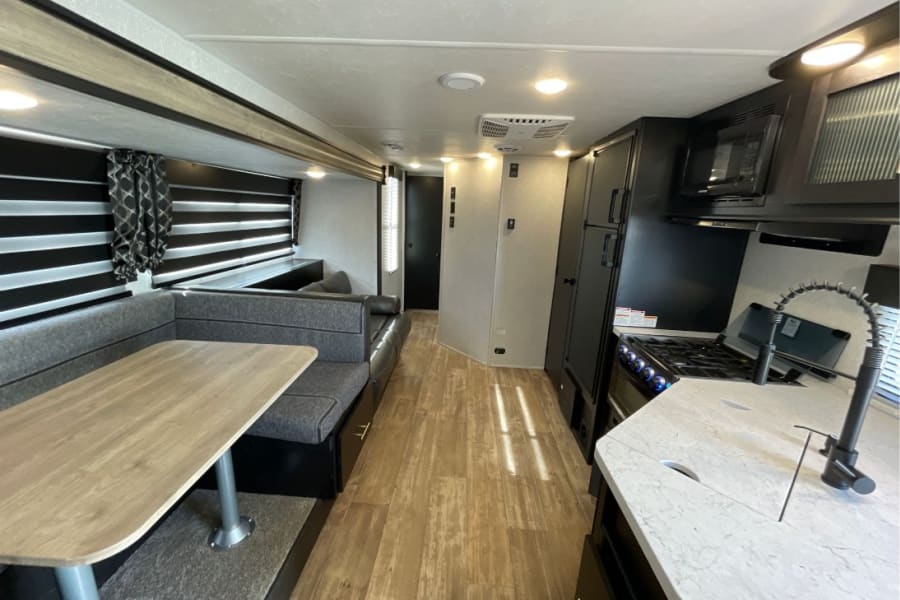Inside a modern RV rental: well-equipped kitchen (stove, sink) and a comfortable dining booth with wood table.