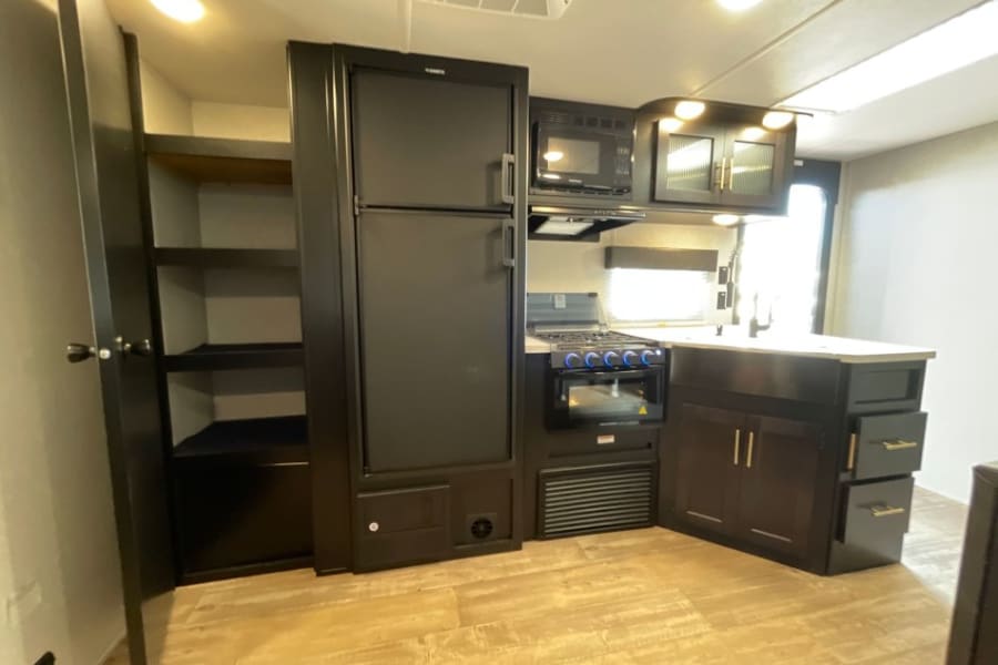 RV rental kitchen interior: fridge, stove, microwave, sink, and ample storage, perfect for your next adventure.