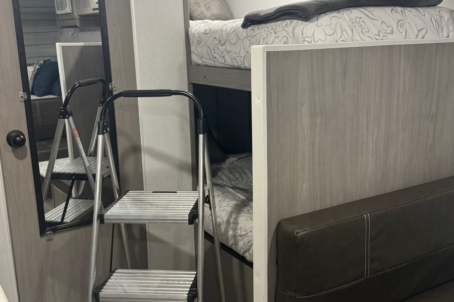 RV rental interior featuring bunk beds, a step ladder, and a full-length mirror, optimizing compact living space.