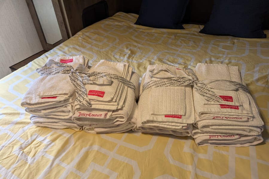Fresh Juicy Couture towels are neatly folded on the bed in this RV rental, ready for your comfortable travels.