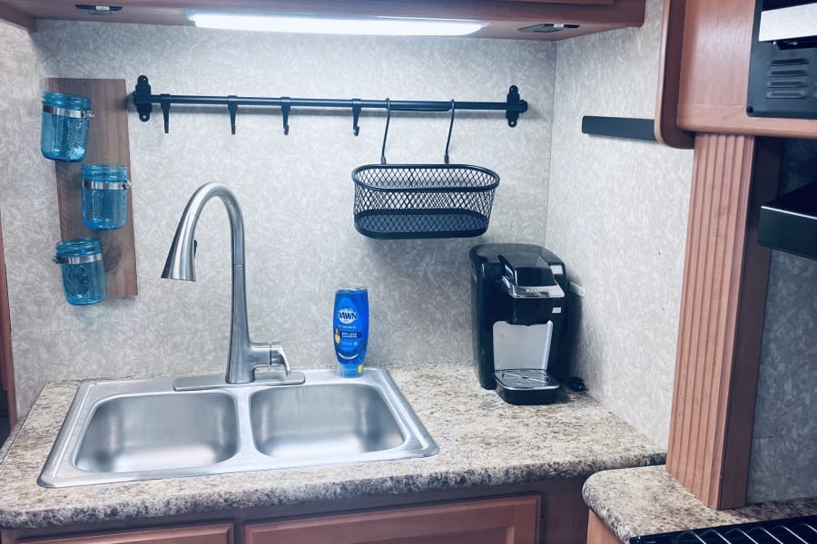 An RV rental kitchen features a double sink, Keurig, and practical wall-mounted storage solutions.