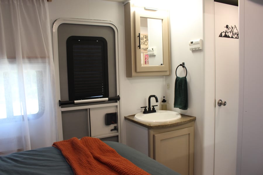 This RV rental's compact interior features a cozy bed, sink vanity, and windowed entry door.