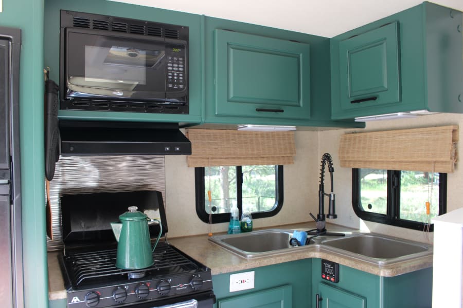 Inside an RV rental: a modern teal kitchen area featuring microwave, stove, sink, and ample storage cabinets.