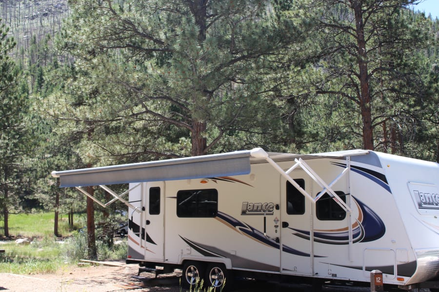 A white RV rental with awning extended at a sunny forest campsite. Explore nature!