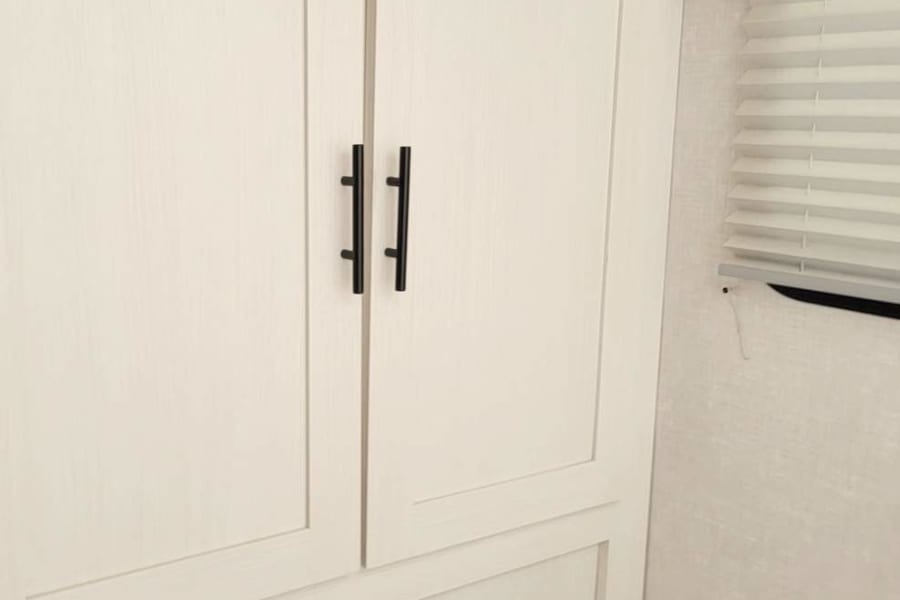 White cabinets & black handles offer storage in this modern RV rental interior. Window with blinds visible.