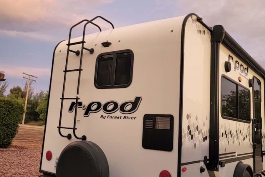 Experience travel freedom! This r-pod RV rental, a compact travel trailer with a ladder and spare tire, is parked under an evening sky.