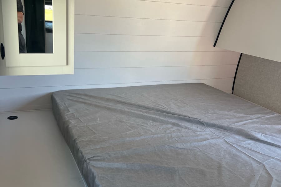 Cozy RV rental bedroom with shiplap walls, comfortable bed, and mirror cabinet for your road trips.