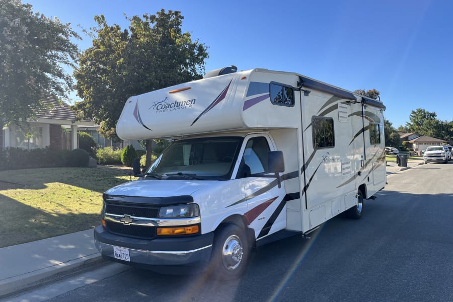 Bright white Coachmen Freelander RV rental parked street-side in a sunny residential neighborhood.