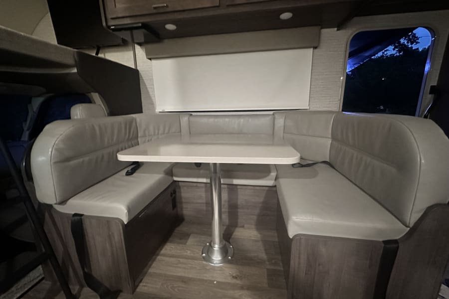 An rv rental dinette with cozy U-shaped seating, a white table, and wood-look flooring.