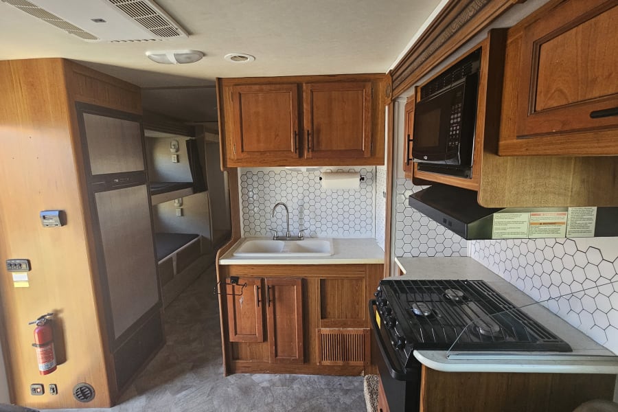 Explore this RV rental's cozy kitchen with a modern backsplash, microwave, stove, and convenient bunk beds visible.