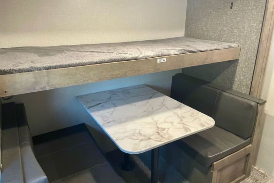 RV rental: Compact interior with a top bunk bed (200 lbs limit) over a dinette featuring a marble-look table & dark gray benches.