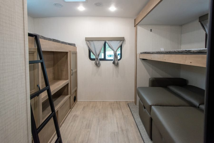 RV rental interior featuring bunk beds, a ladder, a window, and a convertible sofa, ideal for travel.