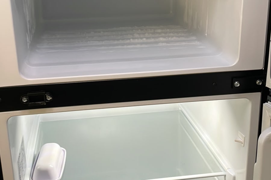 Empty, clean RV rental refrigerator and freezer, with organizing bins. Frost is visible in the top freezer section.