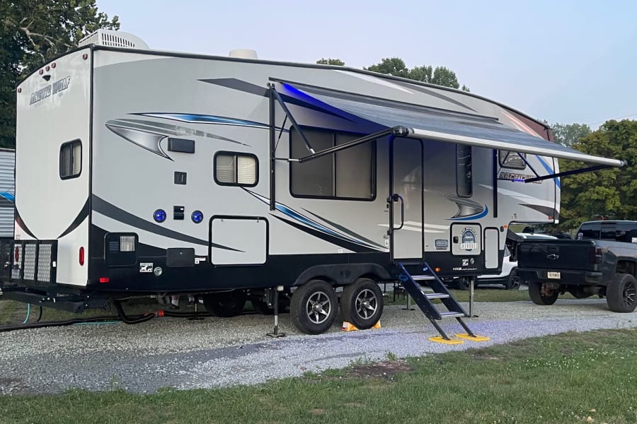 An inviting RV rental, featuring an extended awning and blue lights, parked for a relaxing camping getaway.