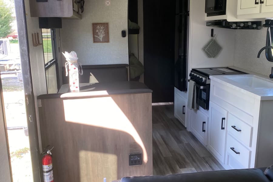 Bright, modern RV rental interior. Features a clean kitchen with stove, microwave, sink, and dining booth. Ready for travel adventures.